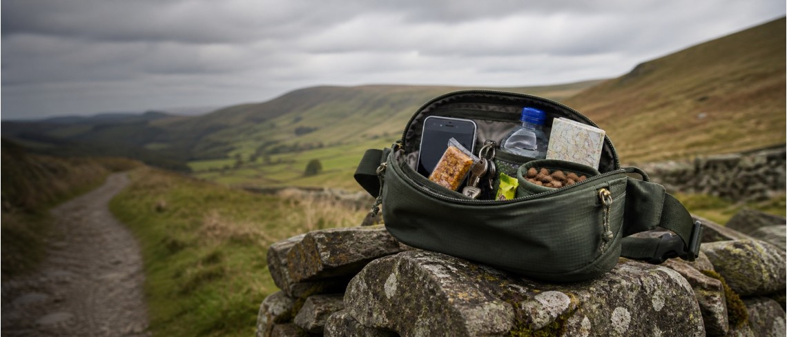 Hiking waist pack with phone, keys, snacks and water bottle on a countryside trail