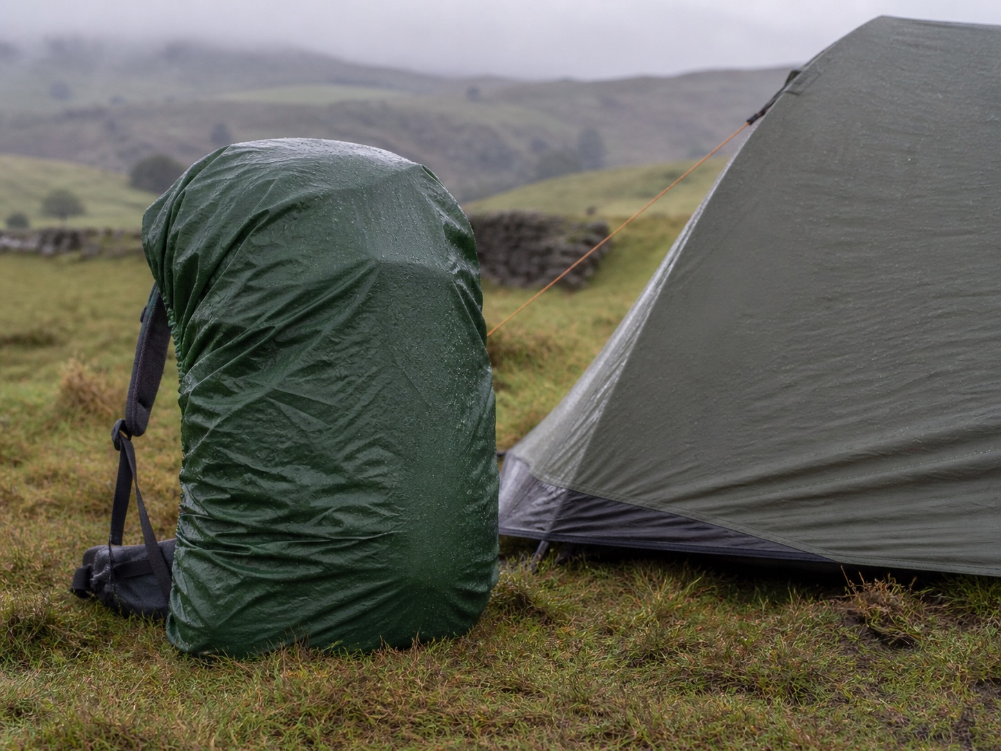 Hiking backpack with rain cover beside a wet campsite